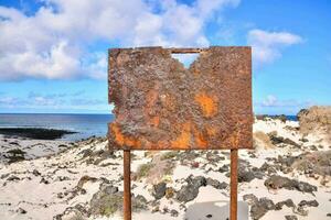 a rusty sign on the beach near the ocean photo