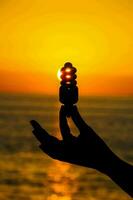 a person holding a light bulb over the ocean at sunset photo