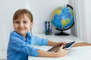 linda pequeño niña es sentado a mesa con su ordenador portátil y estudiando en línea foto