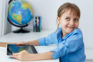 linda pequeño niña es sentado a mesa con su ordenador portátil y estudiando en línea foto