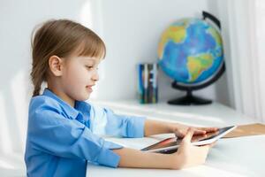 Cute little girl is sitting at table with her laptop and studying online photo