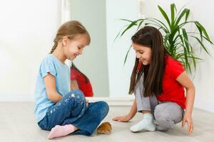 two little girls play with a hamster on the floor at home photo