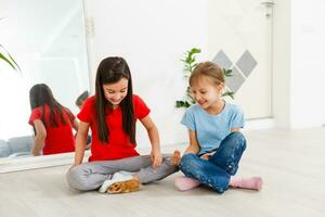 two little girls play with a hamster on the floor at home photo