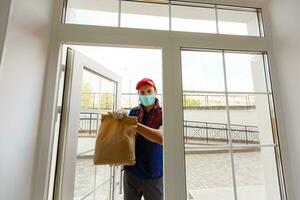 Young courier with thermo bag near the entrance home. Food delivery service photo