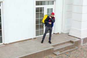 Delivery Man standing with yellow thermo backpack for food delivery near the entrance home with empty space to copy paste photo