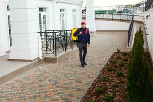 Portrait of a cheerful delivery man standing with yellow thermo backpack for food delivery on the street outdoors photo