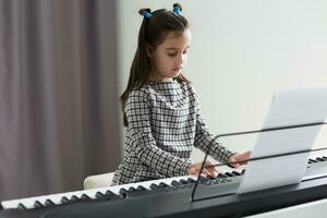 Cute little girl plays on piano, synthesizer. Training. Education. School. Aesthetic training. Elementary classroom. photo