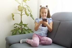 niños, tecnología y comunicación concepto - sonriente niña mensajes de texto en teléfono inteligente y acostado en cama a hogar foto