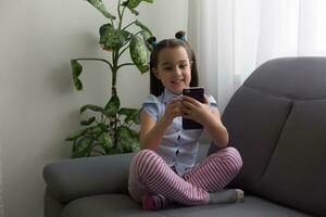 children, technology and communication concept - smiling girl texting on smartphone and lying in bed at home photo