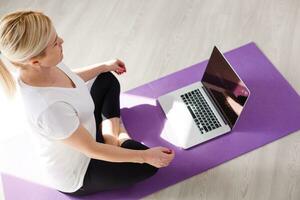 Beautiful young woman training online at home on laptop computer, copy space. Full length portrait. Yoga, pilates, working out exercising photo