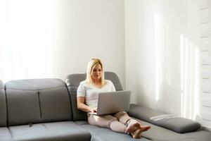 Woman using a laptop while relaxing on the couch photo