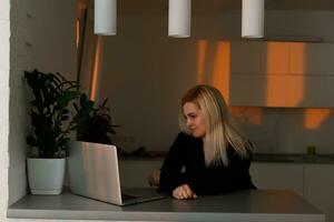 young pretty girl sitting near the window with a laptop, she uses the computer at home on the windowsill, a woman freelance, copy space for text photo