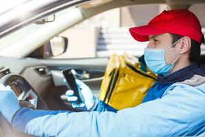 food delivery man in a protective mask and gloves with a thermo backpack near a car during the quarantine period photo