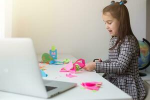 Beautiful little girl cutting paper with scissors on the art lesson class. Children education concept. Kids crafts.Back to schoo photo