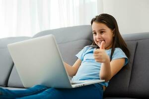 hogar, ocio, tecnología y Internet concepto - pequeño estudiante niña con ordenador portátil computadora a hogar foto