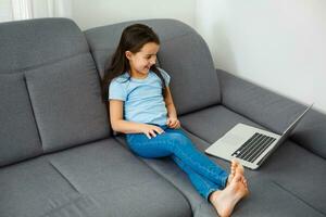 home, leisure, technology and internet concept - little student girl with laptop computer at home photo