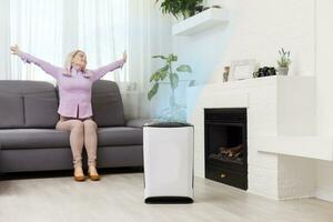 Young woman relaxing on the couch while air humidifier or purifier working on the foreground. Controlling it with a smartphone remotely photo