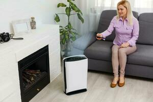 Young woman relaxing on the couch while air humidifier or purifier working on the foreground. Controlling it with a smartphone remotely photo