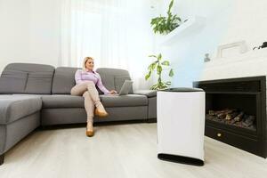 Air purifier in a living room, woman working with laptop with filter for clean room photo