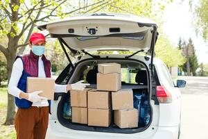 Delivery man holding paper bag with food near the car, food delivery man in protective mask photo