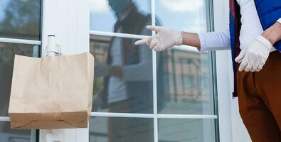 Grocery delivery man wearing medical gloves and face mask. Online shopping and delivery for grocerys, wine and food. Self Quarantine during coronavirus pandemic. Food delivery service courier photo