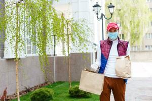 Courier in protective mask and medical gloves delivers takeaway food. Delivery service under quarantine, disease outbreak, coronavirus covid-19 pandemic conditions. photo