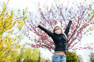 Happy young woman wearing facial mask for virus protection standing outdoors on sunny spring day. photo