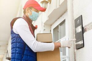 mensajero, entrega hombre en médico látex guantes y máscara sin peligro entrega en línea compras en blanco caja a el puerta durante el coronavirus epidemia, COVID-19. permanecer hogar, seguro concepto. foto