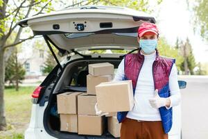 Courier, delivery man in medical latex gloves and mask safely delivers online purchases in white box to the door during the coronavirus epidemic, COVID-19. Stay home, safe concept. photo