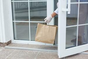 Delivery man holding paper bag with food on white entrance of house background , food delivery man in protective mask photo