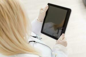 Female runette doctor using tablet, intelligent and lovely woman with the gadget and stethoscope in the white background photo