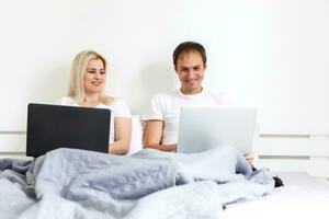 Couple on laptop in bed working on separate computers. Young modern interracial couple, woman, Caucasian man, view with copy space. photo