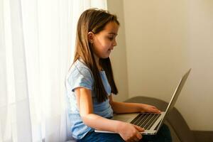 Head shot close up portrait of happy small pupil learning at home. Smiling little child girl enjoying doing lessons in living room. Smart kid schoolgirl looking at camera, studying remotely online. photo