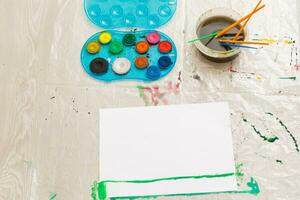 the child draws with a brush with watercolors on a white sheet, a table, a copy place photo