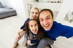 Beautiful young mother, father and their daughter are making selfie using a phone and smiling while sitting at home photo