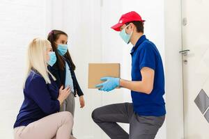 Young woman with little daughter wearing medical mask receiving orderd food from delivery man indoors. Prevention of virus spread photo