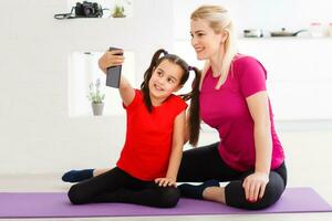 Let's take a picture for social network. Close up portrait of beautiful sportive cute gentle tender mother and daughter wearing sporty clothes making video call via internet connection photo