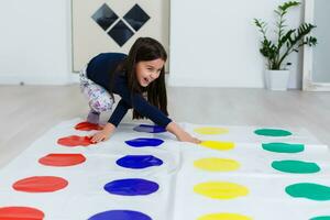 little girl playing on a twister game at home. Girl smiles and looks up photo