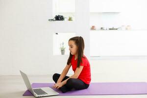 cuarentena a hogar. pequeño niña haciendo yoga en línea en un ordenador portátil durante yo aislamiento cuarentena foto