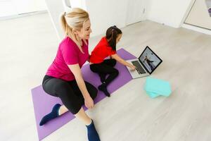 Mother and daughter doing yoga exercises on mat at home. photo