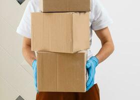 A man a medical mask and blue rubber gloves with a box, a parcel in his hands. Food delivery during the quarantine of the coronavirus pandemic. Home delivery, online order. Online shopping . photo
