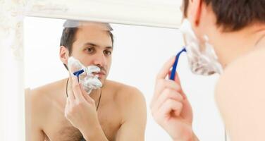 Closeup of handsome young man shaving in bathroom photo