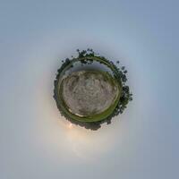 coconut trees in jungle in Indian tropic village on sea shore with fisher boat on little planet in evening sky, transformation of spherical 360 panorama. photo