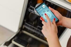 Close-up Of Woman's Hand Showing Dishwasher App On Mobile Phone In Kitchen photo