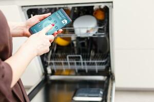 de cerca de mujer mano demostración lavavajillas aplicación en móvil teléfono en cocina foto