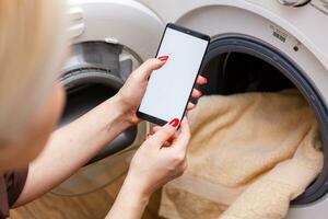 Close-up Of Person Hand Operating Smart Washing Machine Using Mobile Phone App photo