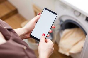 Close-up Of Person Hand Operating Smart Washing Machine Using Mobile Phone App photo