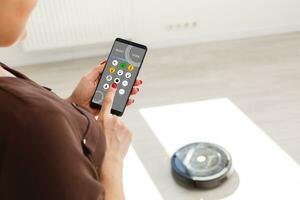 Hand controlling romote of robotic vacuum on wood laminate floor. photo