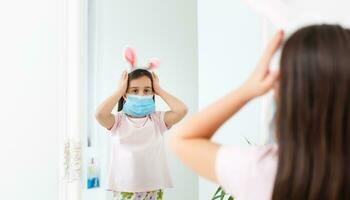 Little caucasian girl with bunny ears and medical mask on her face on a white background. Easter concept. Coronavirus protected photo