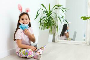 Little caucasian girl with bunny ears and medical mask on her face on a white background. Easter concept. Coronavirus protected photo